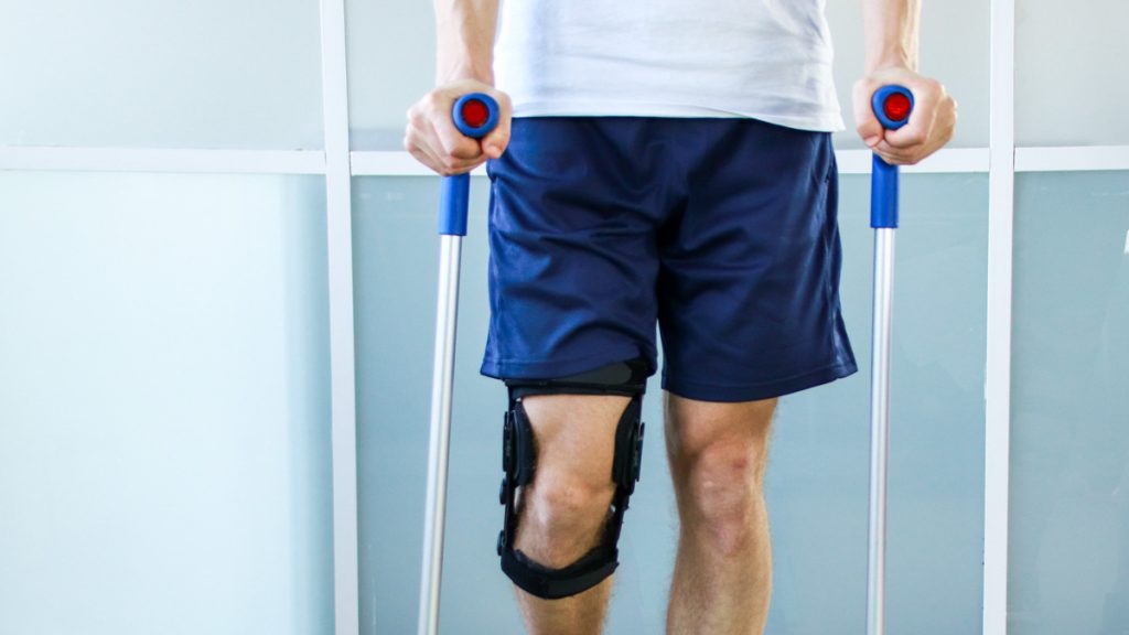 Patient steht an Gehhilfen mit Knie Orthese