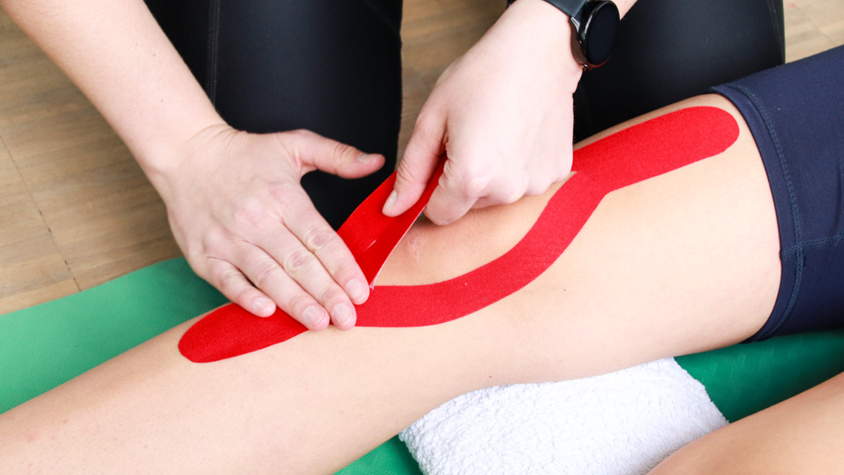 Therapeut bringt rotes Kinesio-Tape an rechtes Knie an